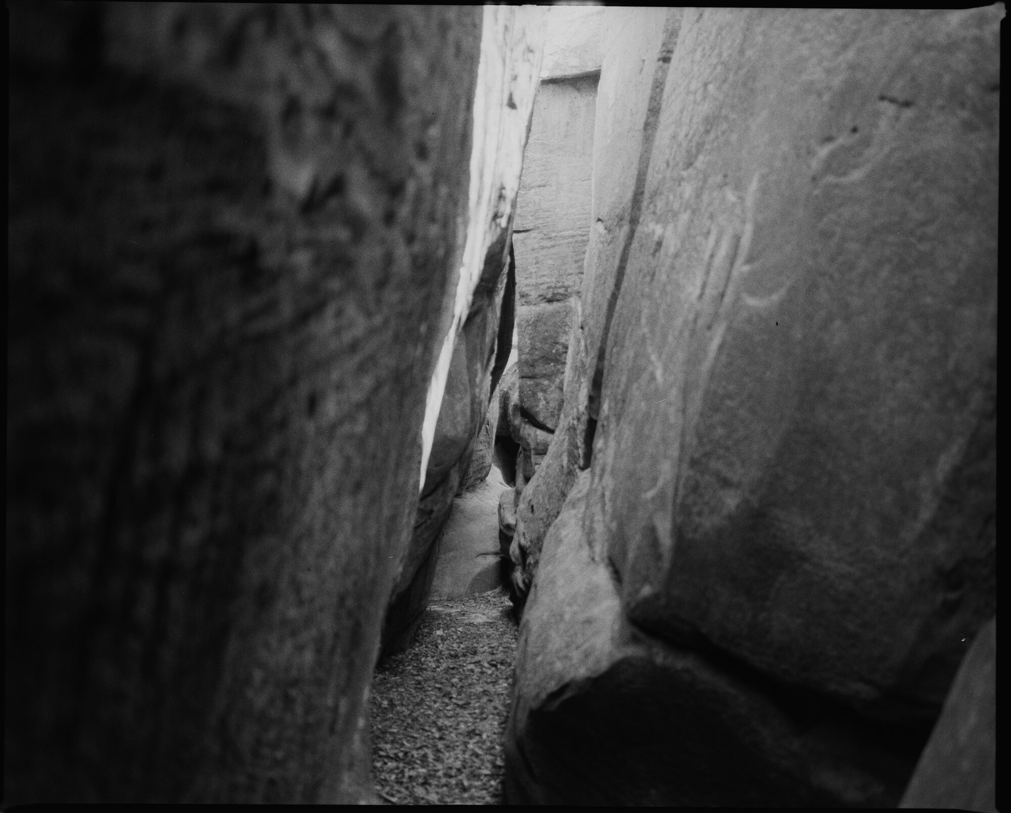 Black and white close-up of weathered rock formations — textured surfaces and deep crevices creating an abstract composition - this is a shot of eroded crevices and sandstone boulders in The Channels Natural Area Preserve. This is a long passage with light at the end.