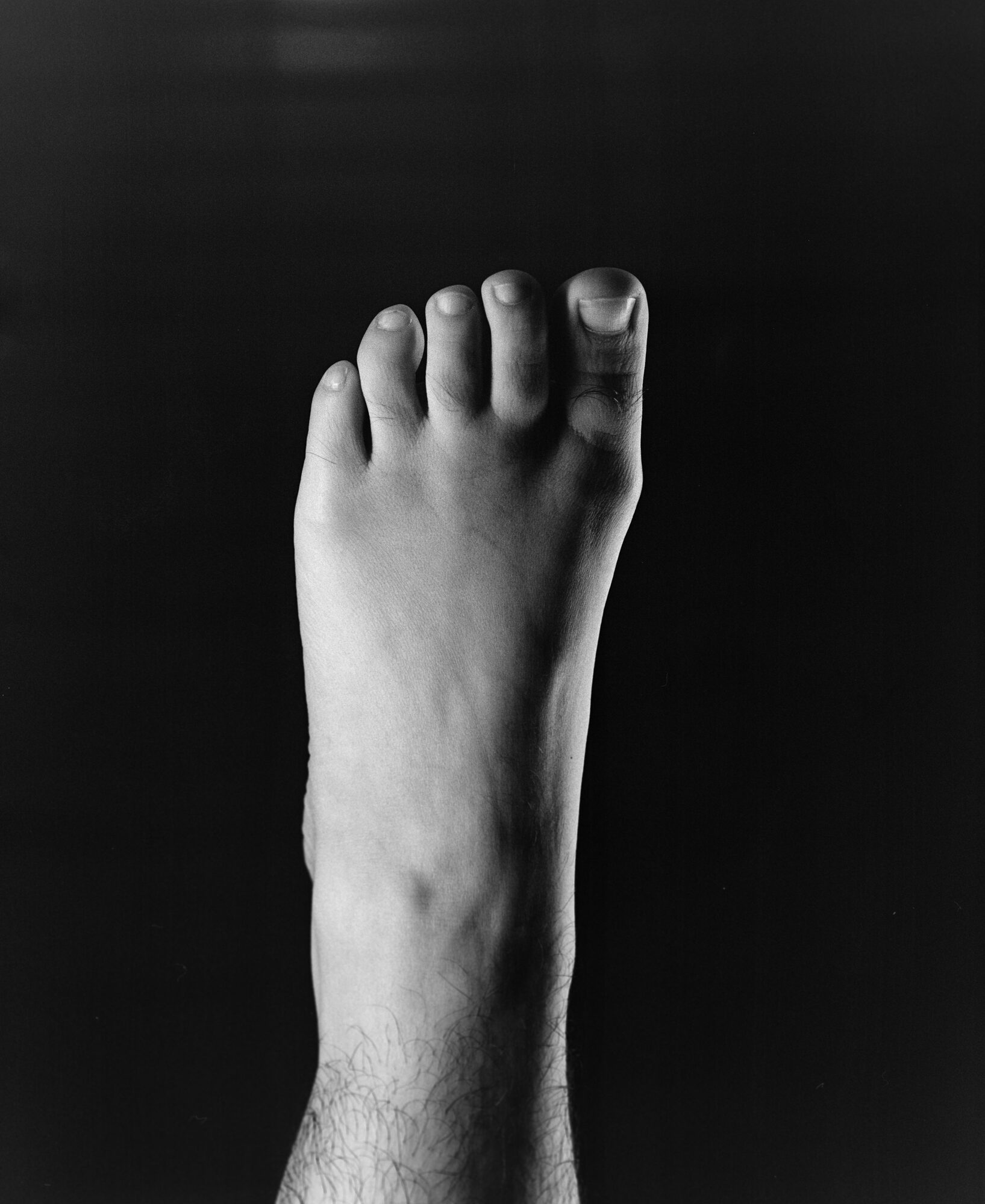 Black and white studio photograph of a bare foot against a black background, sculptural composition