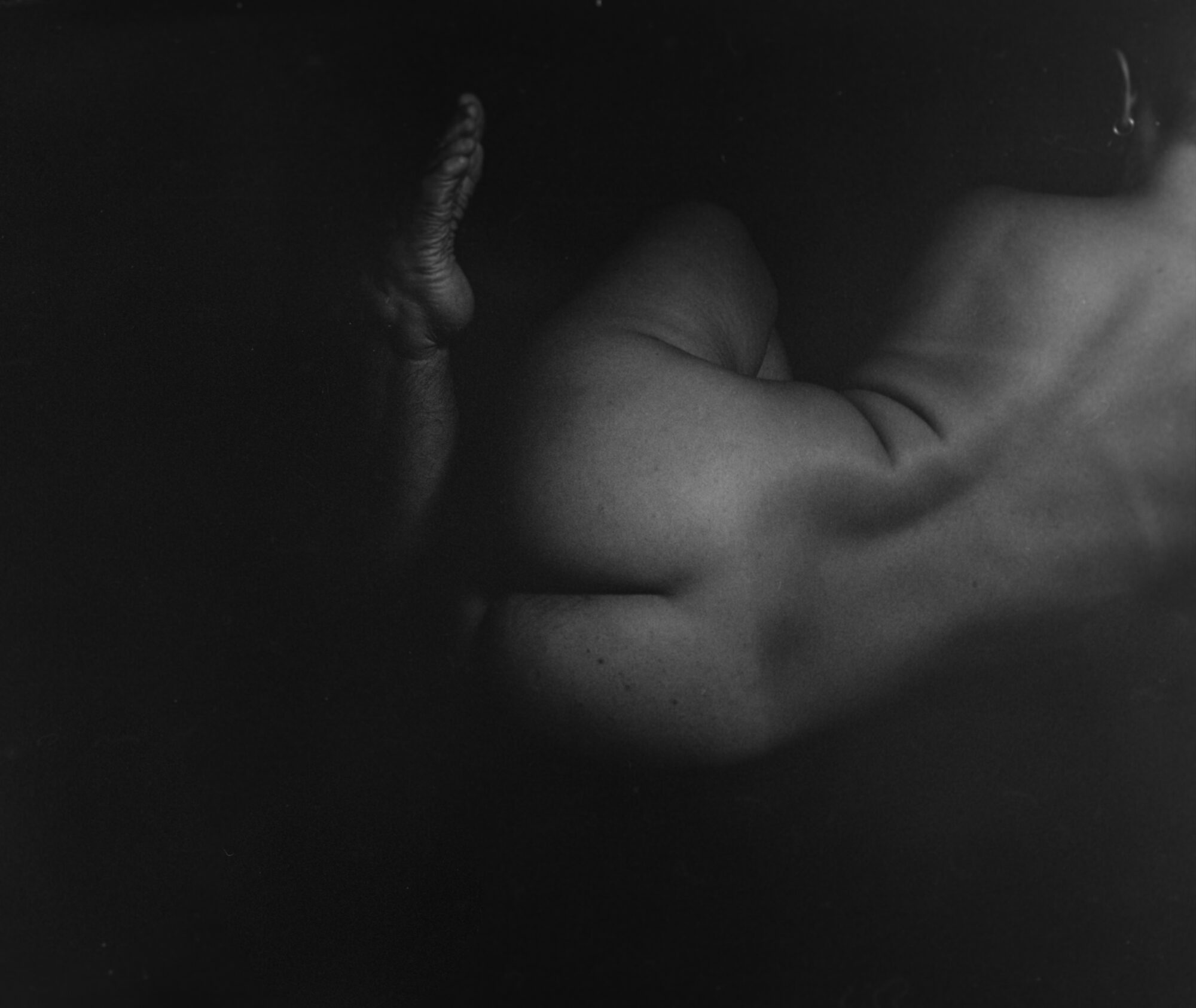 Intimate black and white body study — a shape defined by a foot in the air and her back, thigh and part of her head. All emerging from shadow.